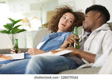 couple leaning back on the sofa holding beers and pizza