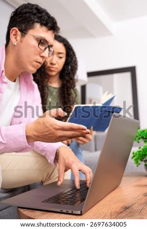 Couple learning at home, man explaining information on laptop, woman listening while holding a book. Focused on education