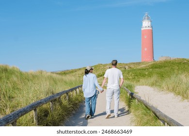 A couple leisurely walks along a path near a picturesque lighthouse on a bright sunny day in Texel, Netherlands. - Powered by Shutterstock