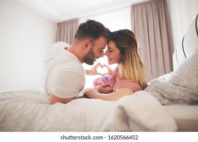 Couple lies in bed and cuddling while showing heart symbol with their hands. - Shutterstock ID 1620566452