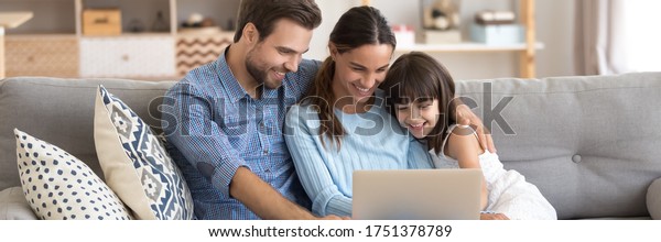 Couple and little daughter sit on sofa using pc\
watching cartoons on-line, surfing internet, buying via e-commerce\
web sites, spend weekend at home. Horizontal photo banner for\
website header design