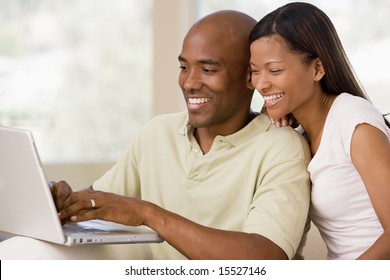 Couple In Living Room Using Laptop And Smiling