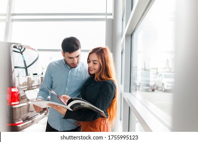 Couple Looking At Car Dealership Catalog