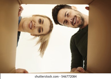 Couple Looking Down At Camera Through Cardboard Box 
