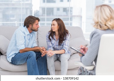 Couple looking to each other during therapy session while therapist watches