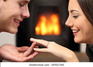 Couple Looking A Engagement Ring After Proposal At Home With A Fire Place In The Background