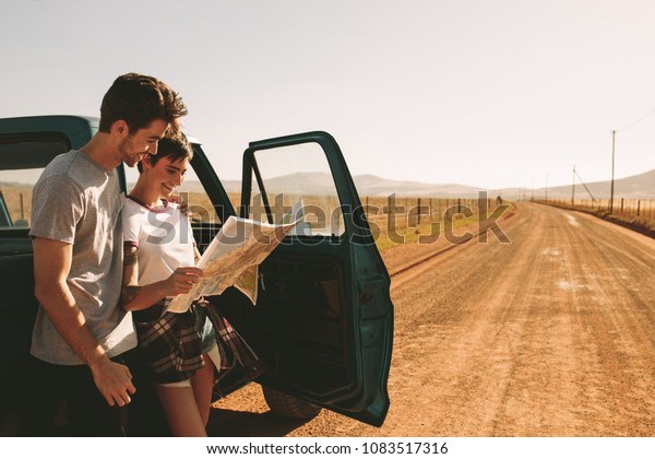 Couple looking at a map for navigation while on a\
road trip on a mud track. Man and woman using a map to navigate\
through the country\
side.
