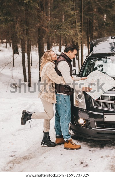 Couple are looking at a map near a car in a winter\
forest, NOISE EFFECT ON\
PHOTOS