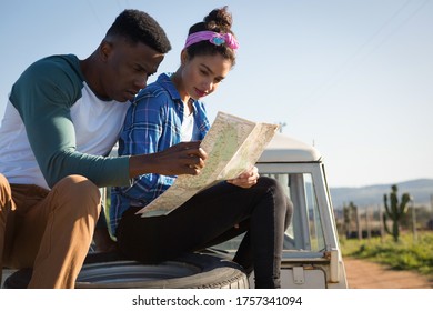 Couple Looking At Map While Sitting On Car Bonnet At Countryside