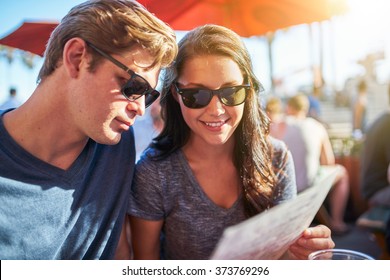 Couple Looking At Menu Seated In Outdoor Restaurant Shot With Selective Focus And Lens Flare