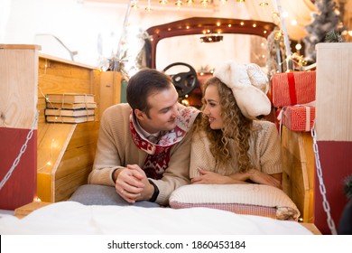 Couple Looking On Each Other And Enjoying Their Time Together In Red Car. Christmas Tree On Background. Magic Lights