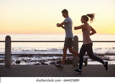 Couple looking at their fitness tracking app while running along the ocean at sunset, fit active lifestyle - Powered by Shutterstock