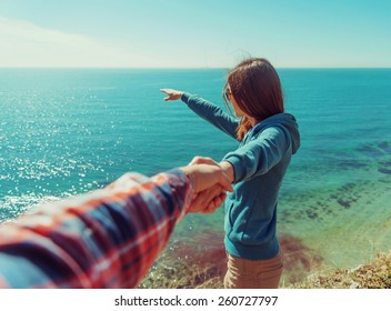 Couple in love. Beautiful young woman holding man's hand and showing him something in distance the sea. Point of view shot
