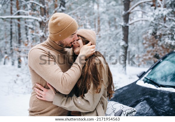 couple in love in beige clothes\
near the car. winter love story. snow-covered pine forest. man and\
woman hugging in the winter forest. car in the\
snow
