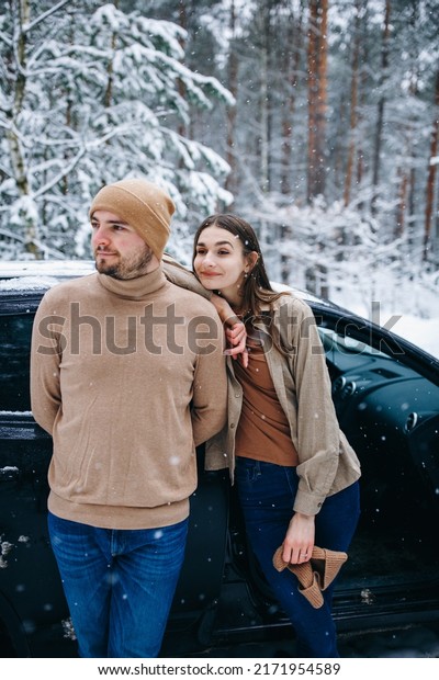 couple in love in beige clothes\
near the car. winter love story. snow-covered pine forest. man and\
woman hugging in the winter forest. car in the\
snow