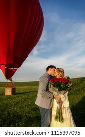 Couple In Love With Bouquet Of Red Roses Kissing On Hot Air Ballon Background. Romantic Date, Marriage Proposal And Honeymoon