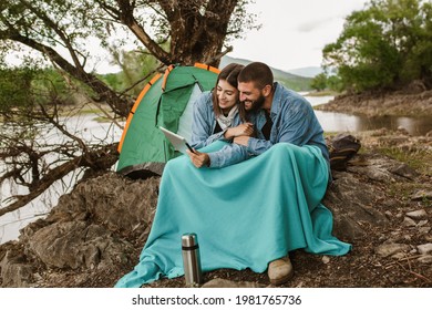 Couple in love camping forest hike.  Couple sitting near tent using digital tablet. - Powered by Shutterstock