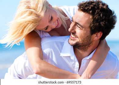 Couple In Love - Caucasian Man Having His Woman Piggyback On His Back Under A Blue Sky On A Beach