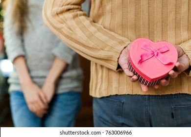 Couple In Love Celebrate Valentine's Day. Man Making Surprise On Holiday To His Pretty Wife. Wife Close Her Eyes And Waiting For Present. Concept Of Happy Valentine's Day