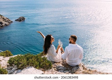 A couple in love celebrates their engagement on the seashore. A beautiful couple drinks champagne by the sea. Honeymoon trip. Lovers on the beach. Wedding travel. Couple on vacation. Copy space
