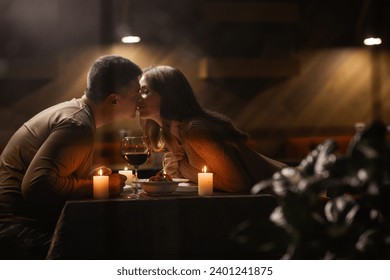 Couple in love celebrating Valentine's day having dinner at home, kissing, view through the window. Copy space