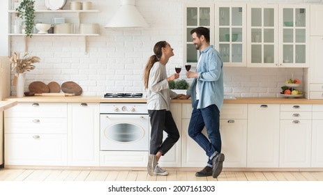 Couple in love chatting standing in cozy kitchen celebrate life event drinking red wine. Romantic date, relationships, new house homeowners family, repairs services, kitchen furniture services concept