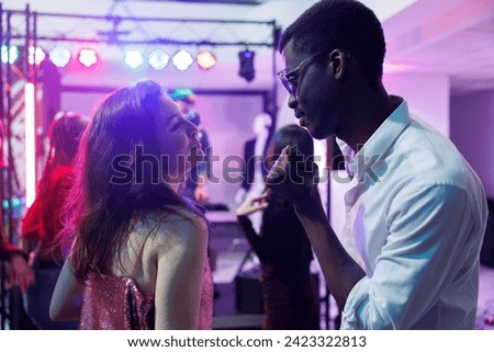 Couple in love dancing and clubbing while attending disco party in nightclub. Young diverse boyfriend and girfriend celebrating, moving to music rhythm on dancefloor illuminated with stage spotlights