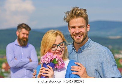Couple in love dating while jealous bearded man watching wife cheating him with lover. Lovers hugs outdoor flirt romance relations. Couple romantic date lovers bouquet flowers. Infidelity concept.