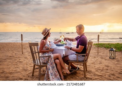 Couple in love drinking champagne wine on romantic dinner at sunset on the beach with yachts on background. Young couple celebration anniversary, clink glasses at served table on sea sandy coastline. - Shutterstock ID 2172481687