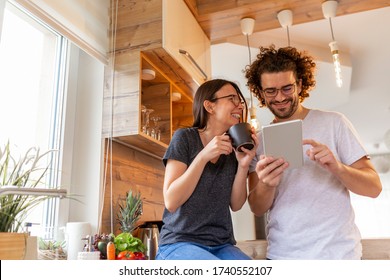 Couple in love drinking coffee and reading news using a tablet computer in the kitchen - Powered by Shutterstock