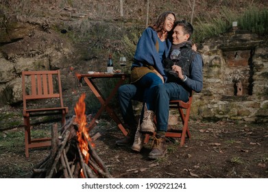 Couple In Love Drinking Wine And Having Fun In A Garden With Fire. People Sitting At The Table And Woman On Man's Legs