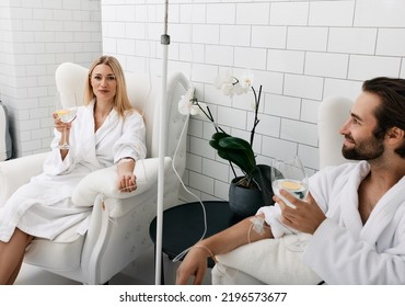 Couple in love during intravenous vitamin therapy. Beautiful woman with her boyfriend with glasses of refreshing drink with lemon in medical clinic for detox their organisms