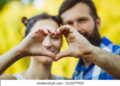 Couple in love gesturing heart with fingers. Portrait of brunette and her handsome bearded boyfriend in park