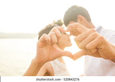 Couple in love gesturing heart with fingers against sunrise