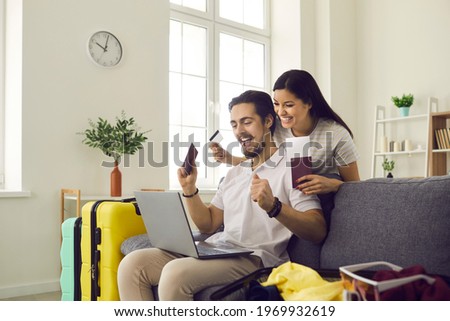 Couple in love getting ready for holiday trip using airline website to book tickets online. Happy man and woman excited about travel vacation abroad sitting on couch at home looking at laptop screen