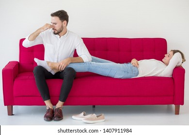couple in love girlfriend lying down on  red sofa boyfriend massage her feet with unpleasant  Foot odor  at home, indoors . Foul-smelling