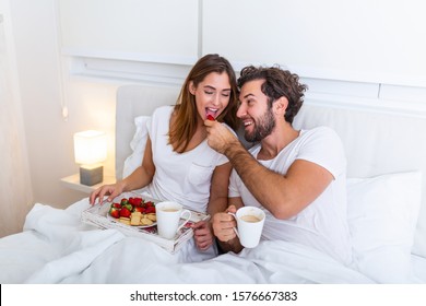 Couple in love having breakfast in bed. Young caucasian couple having romantic breakfast in bed. Female and male , two cups of coffee, fruits and colorful biscuits. - Powered by Shutterstock