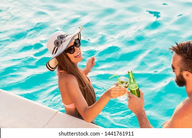 Couple in love having fun at a poolside summer party, standing in water next to the swimming pool edge, making a toast - Powered by Shutterstock