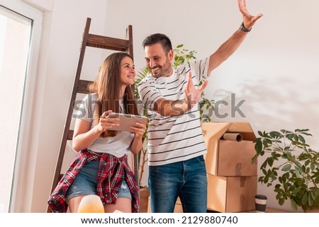 Couple in love having fun while moving in new home, searching for apartment redecoration ideas using tablet computer