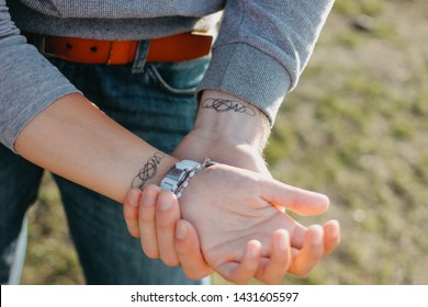 Couple In Love Holding Hand In Hand. Paired Tattoo Initials On The Arms