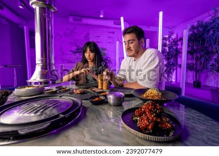 a couple in love in a korean restaurant with a grill and a hood above the table tastes a variety traditional dishes with chopsticks food concept