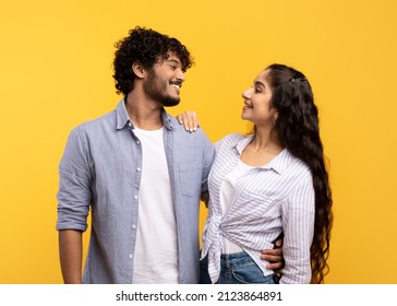 Couple in love. Loving couple embracing, looking and smiling to each other, standing over yellow studio background. Family photo of cheerful young hindu spouses