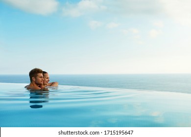 Couple In Love At Luxury Resort On Romantic Summer Vacation. People Relaxing Together In Edge Swimming Pool Water, Enjoying Beautiful Sea View. Happy Lovers On Honeymoon Travel. Relationship, Romance