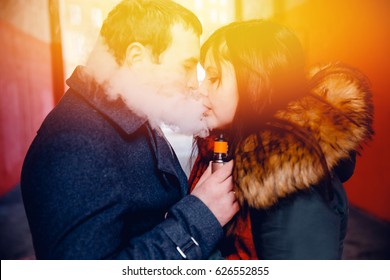 couple in love a man and a girl kiss and smoke electronic cigarettes vape mod and drip. There are clubs of steam. Concept smoking in public places.