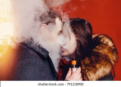 couple in love a man and a girl kiss and smoke electronic cigarettes vape mod and drip. There are clubs of steam. Concept smoking in public places.