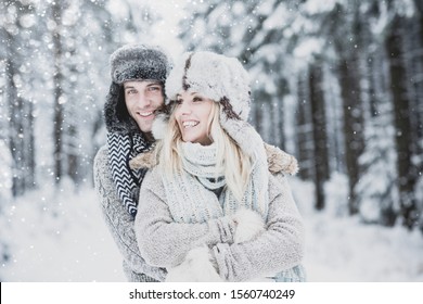 couple in love, man and woman with warm clothes, cap and scarf against winter backdrop in snowy landscape