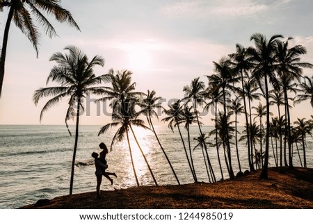 A couple in love meets a sunset on the sea among the palm trees. Man and woman at sunset. Honeymoon on the Islands. Man and woman meet sunset. Happy loving couple. Silhouette lovers. Wedding travel