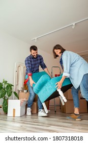 Couple In Love Moving In Together, Having Fun While Carrying An Armchair And Setting Up The New Furniture Arrangement