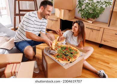 Couple in love moving in together, taking a break from unpacking cardboard boxes, having fun while eating pizza for lunch - Powered by Shutterstock