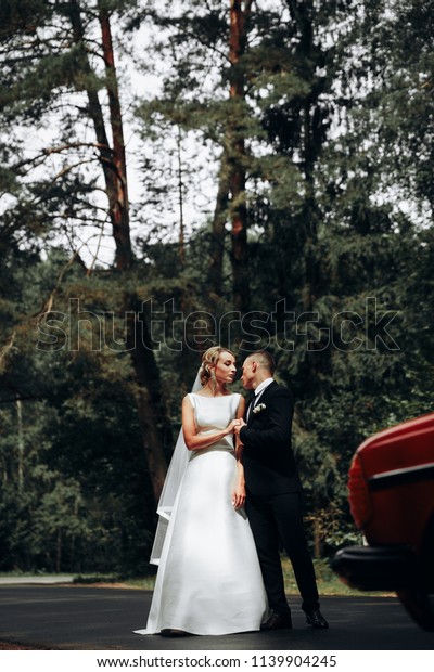 A couple in love near a retro car.Newlyweds in the\
woods on the road.A couple of red and a retro car.Wedding\
photo.Bride and groom.